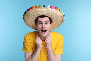 Young man in Mexican sombrero hat on light blue background