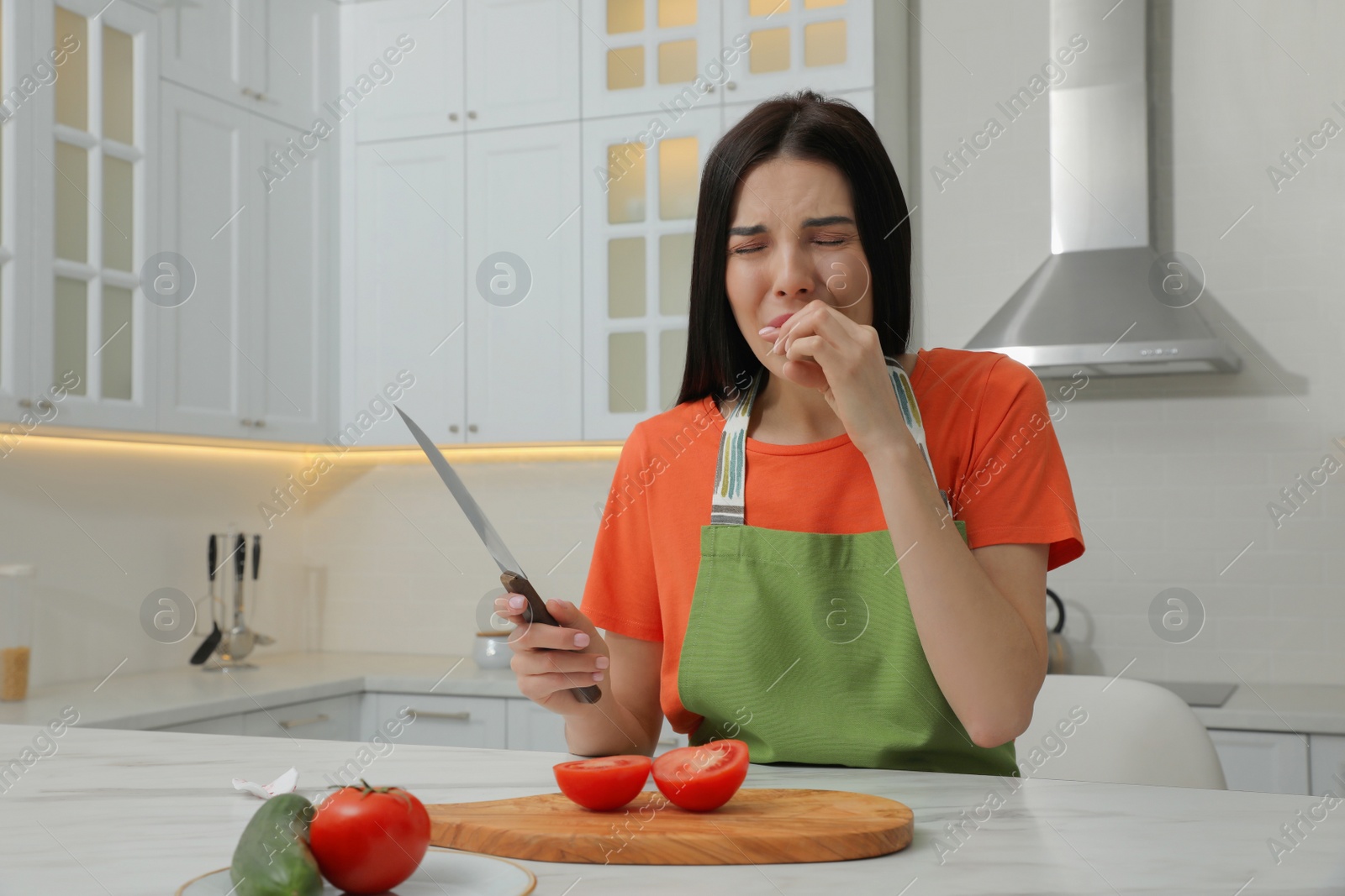 Photo of Young woman cutting finger with knife while cooking in kitchen