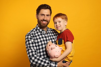 Photo of Father and his son with ceramic piggy bank on orange background