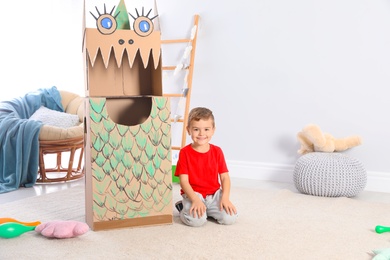 Photo of Cute little boy playing with cardboard dragon at home. Space for text