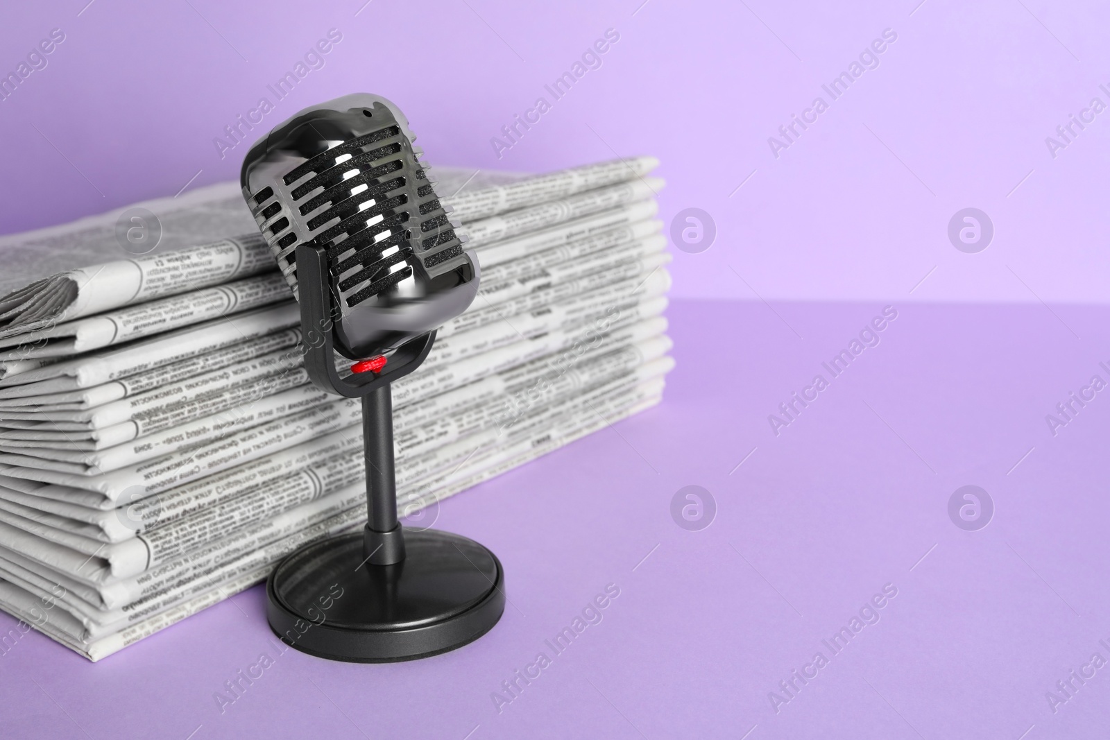 Photo of Newspapers and vintage microphone on light violet background, space for text. Journalist's work