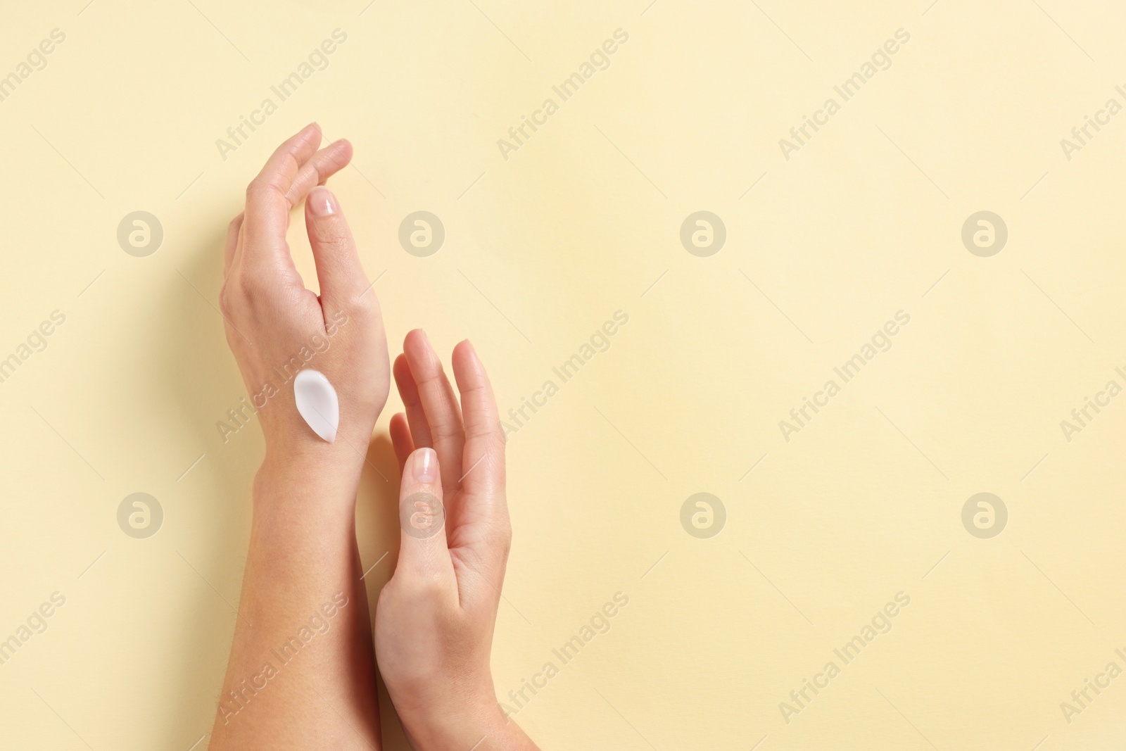 Photo of Woman with cosmetic cream on hand against beige background, top view. Space for text