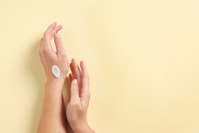 Woman with cosmetic cream on hand against beige background, top view. Space for text