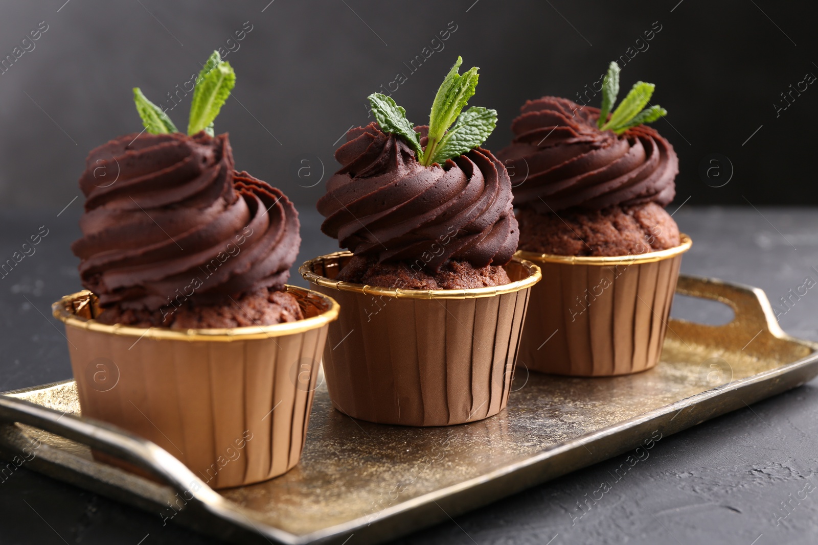 Photo of Delicious chocolate cupcakes with mint on black textured table