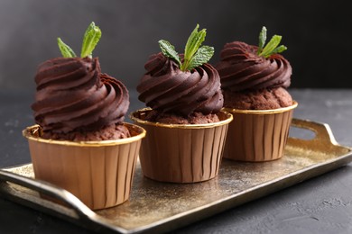 Photo of Delicious chocolate cupcakes with mint on black textured table