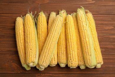 Tasty ripe corn cobs on wooden background, top view