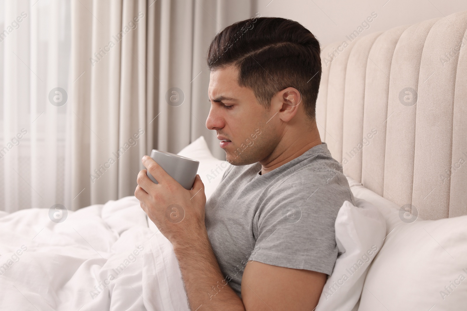 Photo of Sick man with cup of hot drink in bed at home