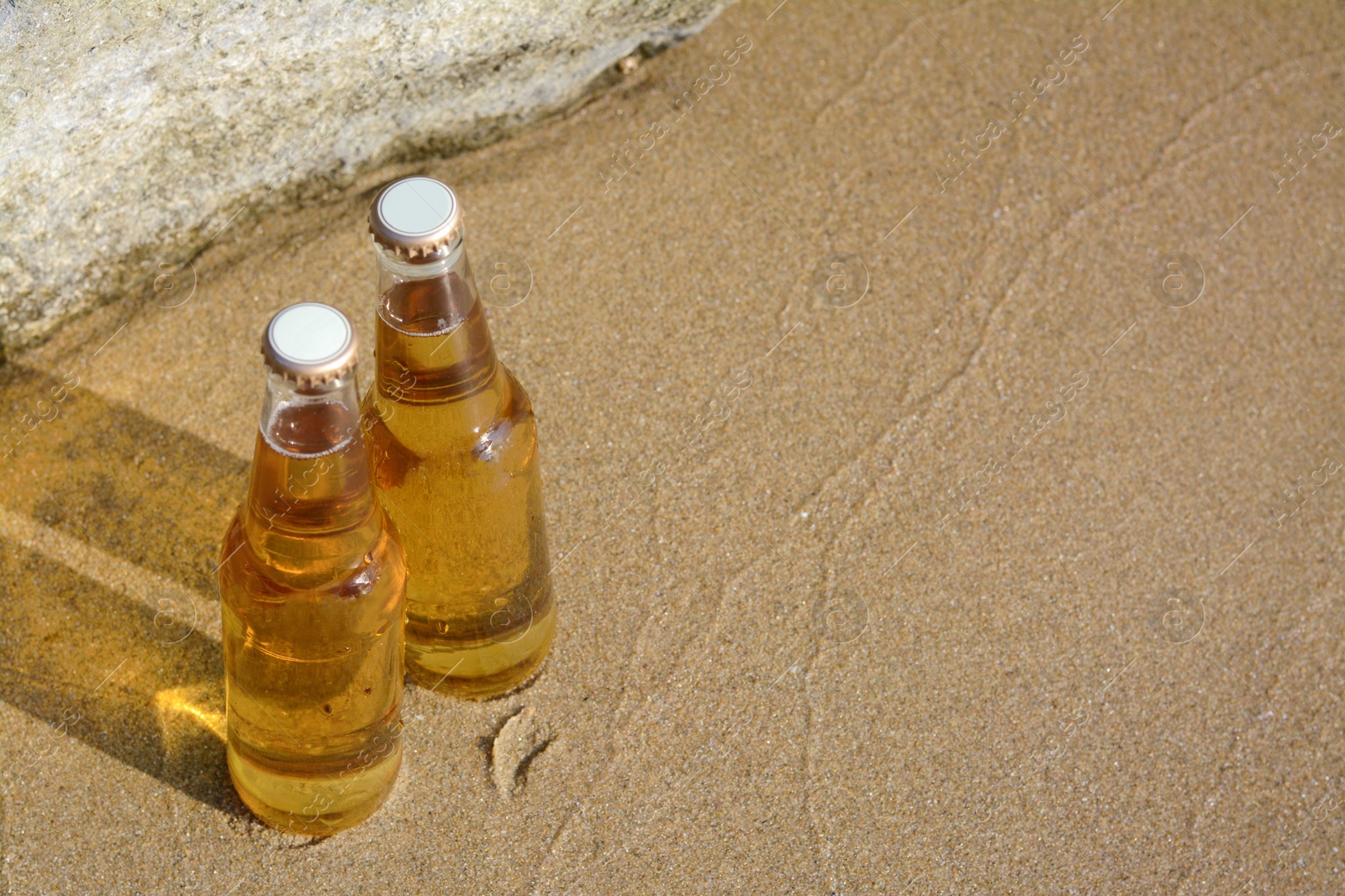 Photo of Bottles of cold beer near rock on sandy beach, above view. Space for text