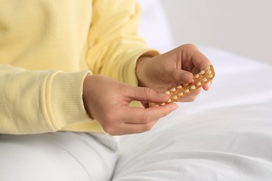 Photo of Woman taking blister of oral contraception pill in bedroom, focus on hands