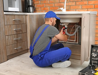 Photo of Professional plumber in uniform fixing kitchen sink