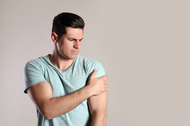 Man suffering from shoulder pain on beige background. Space for text