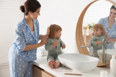 Photo of Mother brushing hair of her little daughter in bathroom