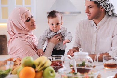 Happy Muslim family with little son at served table in kitchen