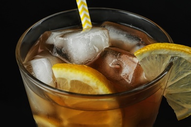 Glass of delicious iced tea against black background, closeup