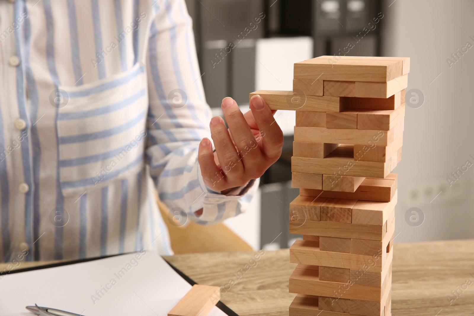 Photo of Playing Jenga. Woman removing block from tower at wooden table indoors, closeup