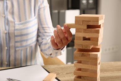 Photo of Playing Jenga. Woman removing block from tower at wooden table indoors, closeup