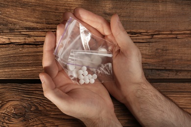 Photo of Man holding plastic bags with drugs on wooden background, top view