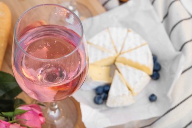 Photo of Glass of delicious rose wine and food on white picnic blanket, closeup