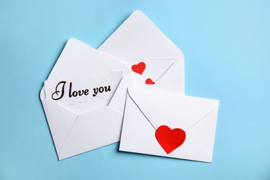 Card with phrase I Love You in envelope and red hearts on light blue background, flat lay