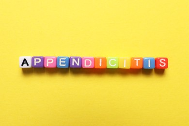 Photo of Word Appendicitis made of color cubes with letters on yellow background, top view