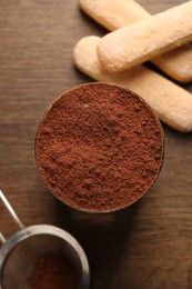 Delicious tiramisu in glass, biscuits and sieve with cocoa powder on wooden table, flat lay