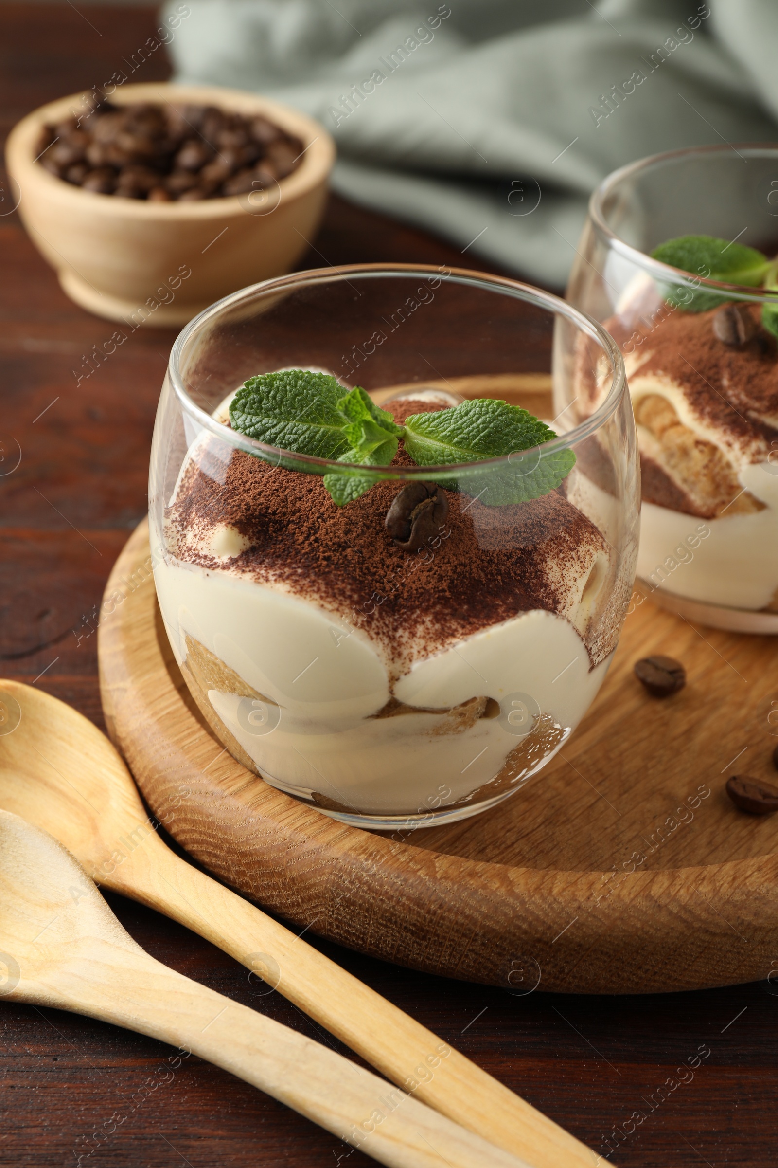 Photo of Delicious tiramisu in glasses, mint leaves, coffee beans and spoons on wooden table