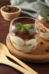 Photo of Delicious tiramisu in glasses, mint leaves, coffee beans and spoons on wooden table