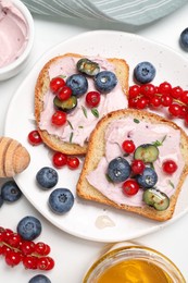 Photo of Tasty sandwiches with cream cheese, berries and honey on white table, flat lay