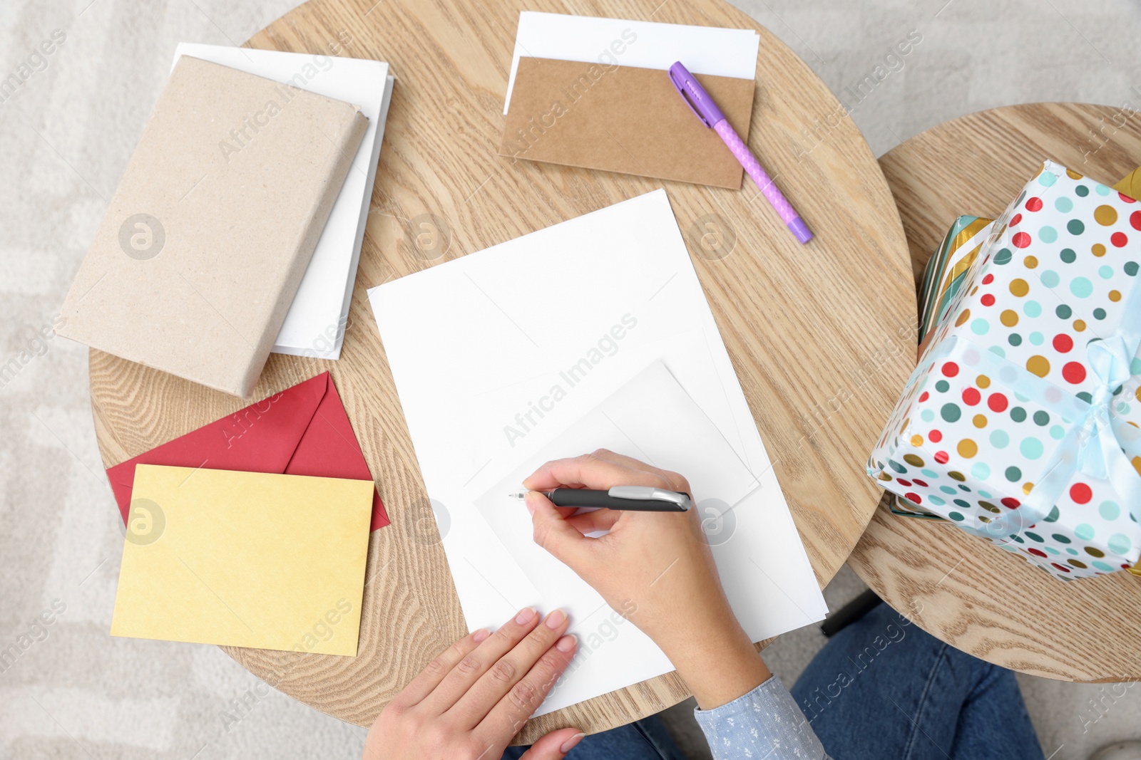 Photo of Young woman writing message in greeting card at wooden table indoors, above view