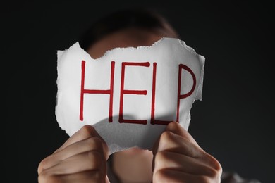 Woman holding piece of paper with word Help on black background, closeup. Domestic violence concept