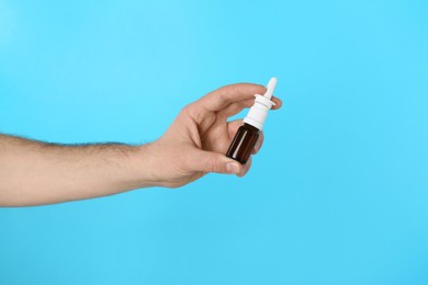 Photo of Man holding nasal spray on light blue background, closeup. Space for text