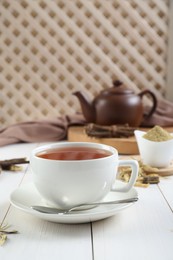 Photo of Aromatic licorice tea in cup and dried sticks of licorice root on white wooden table. Space for text