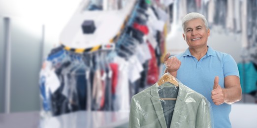Image of Dry-cleaning service. Happy man holding hanger with shirt in plastic bag and showing thumbs up indoors, space for text. Banner design