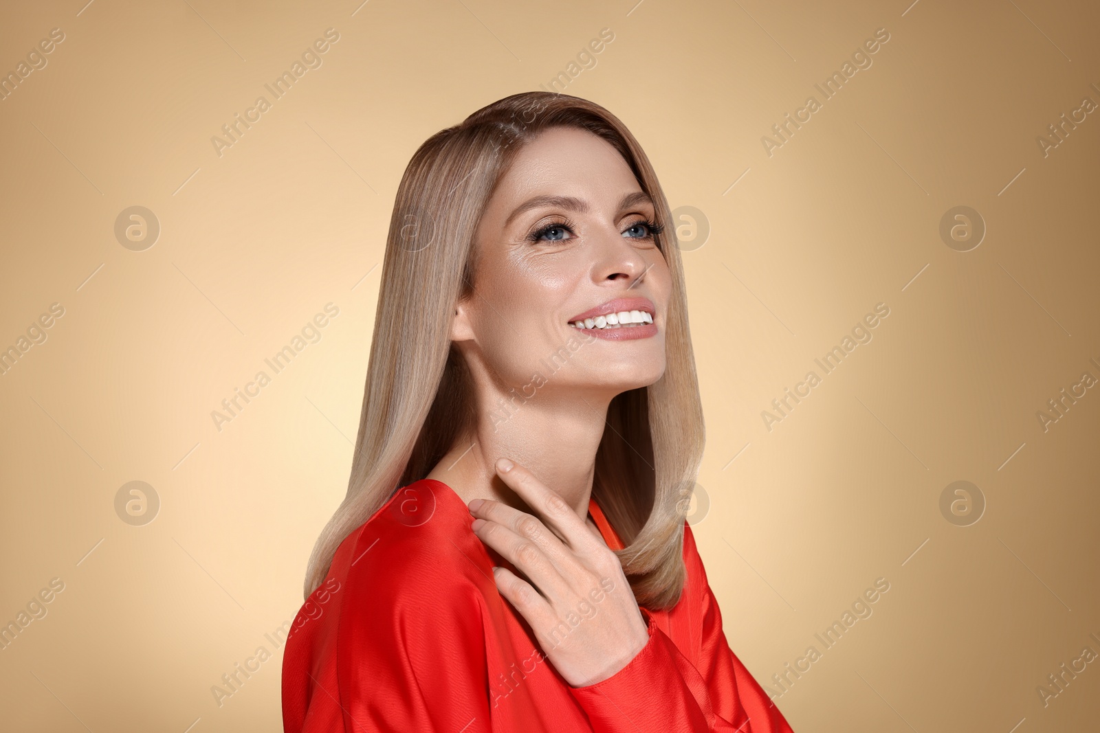 Image of Portrait of stylish attractive woman with blonde hair smiling on dark beige background