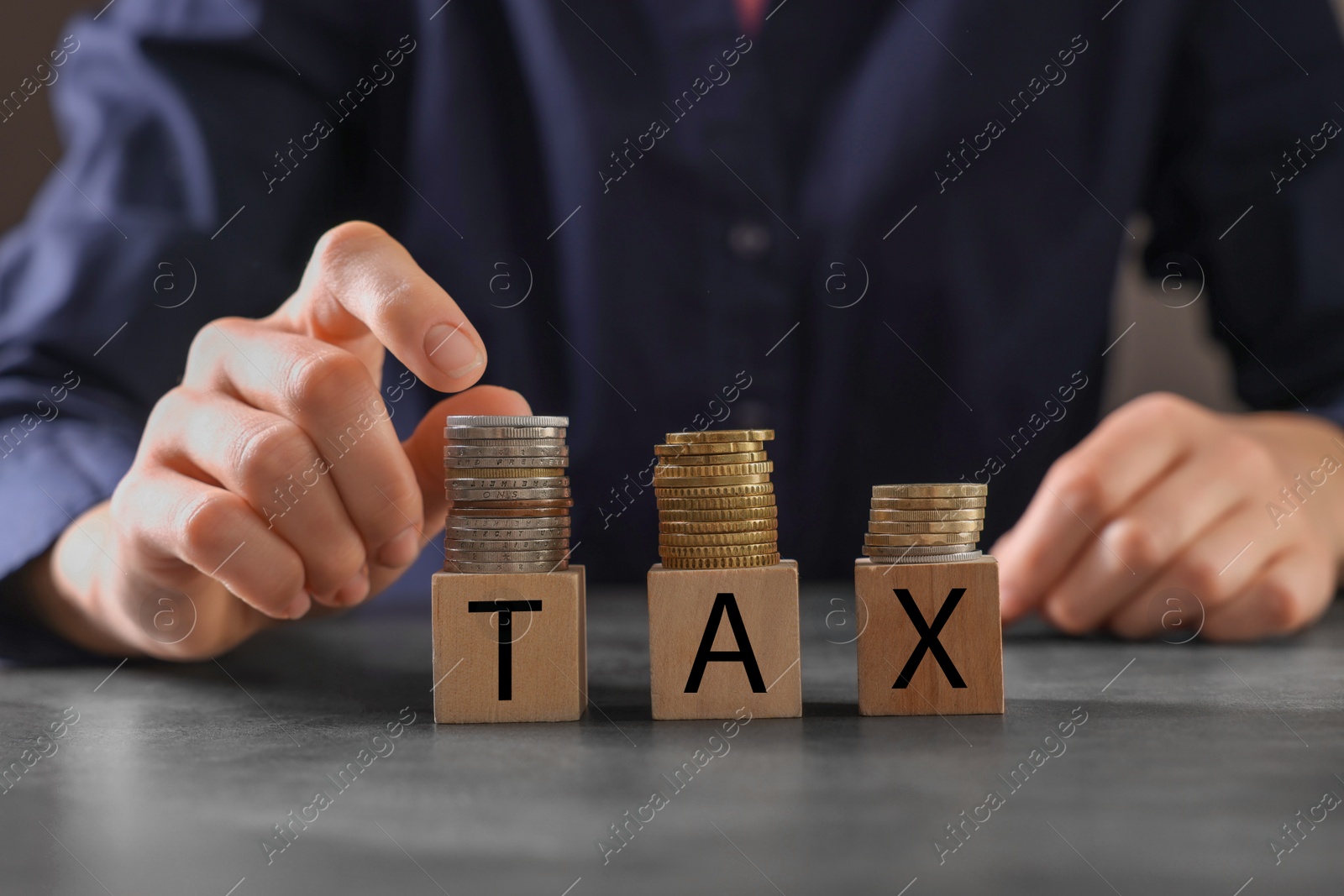 Photo of Woman with word Tax made of wooden cubes and coins at grey table, closeup