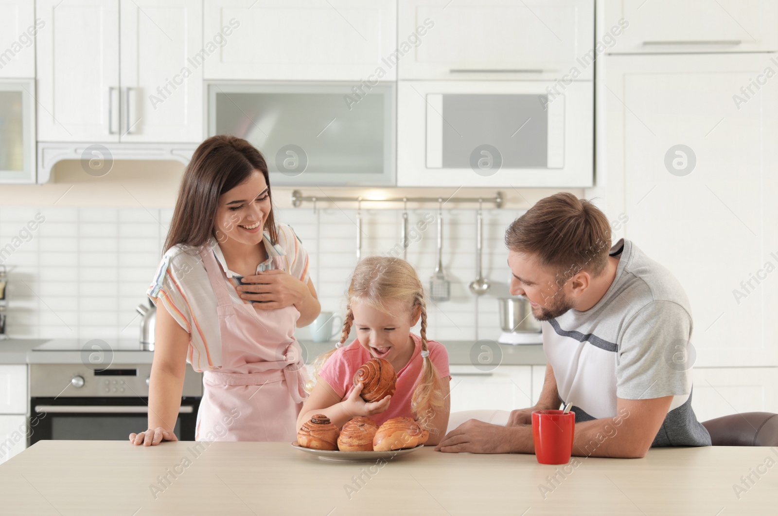 Photo of Happy couple treating their daughter with freshly oven baked bun in kitchen