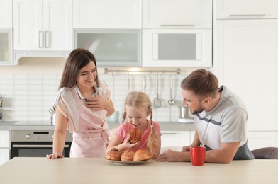 Photo of Happy couple treating their daughter with freshly oven baked bun in kitchen