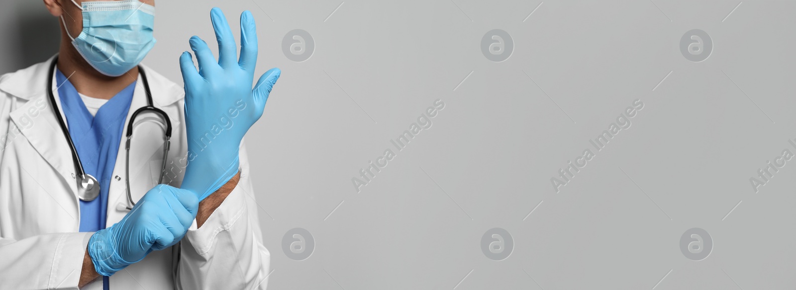 Image of Doctor in protective mask putting on medical gloves against light grey background, closeup. Banner design with space for text  