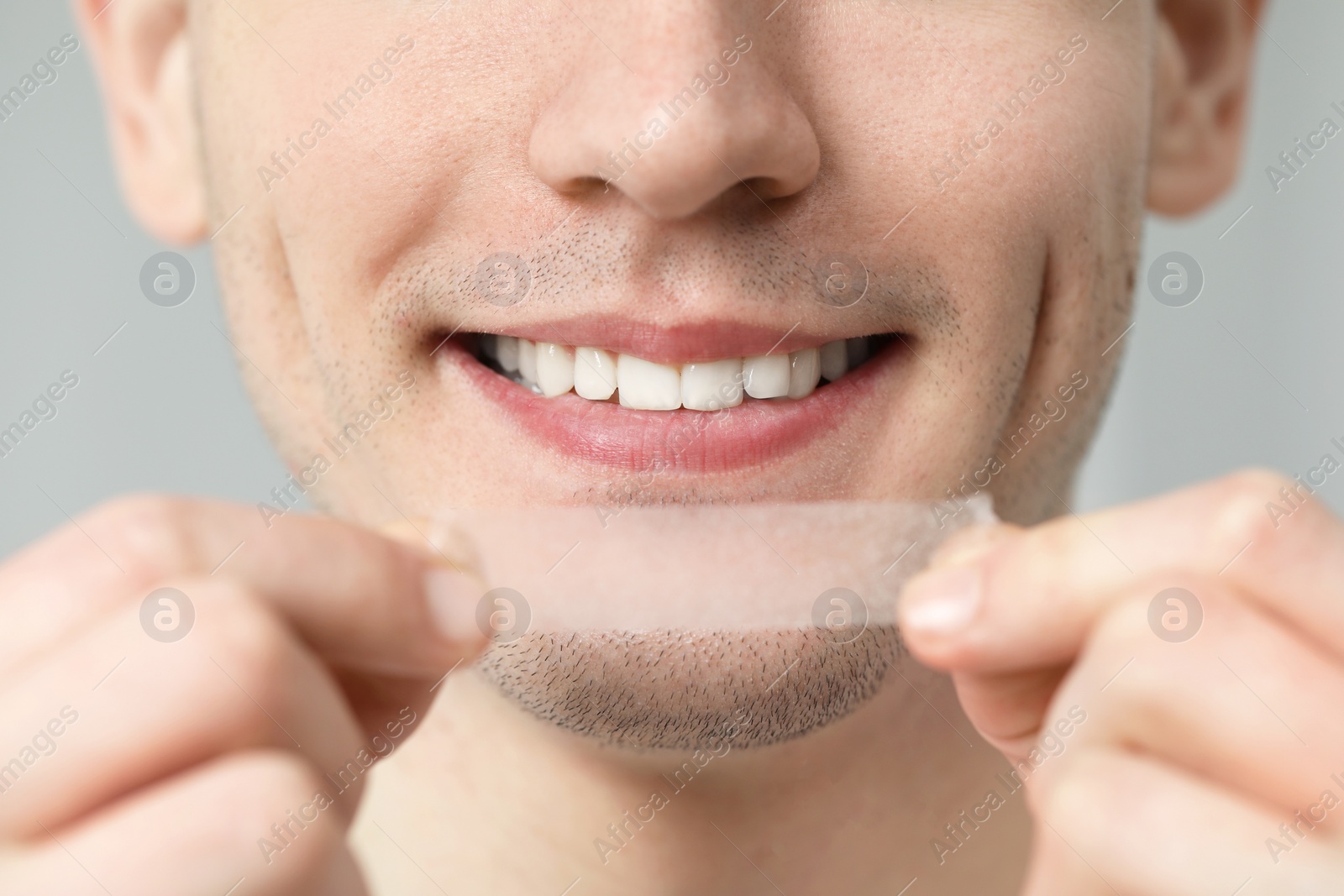 Photo of Young man with whitening strip on light grey background, closeup