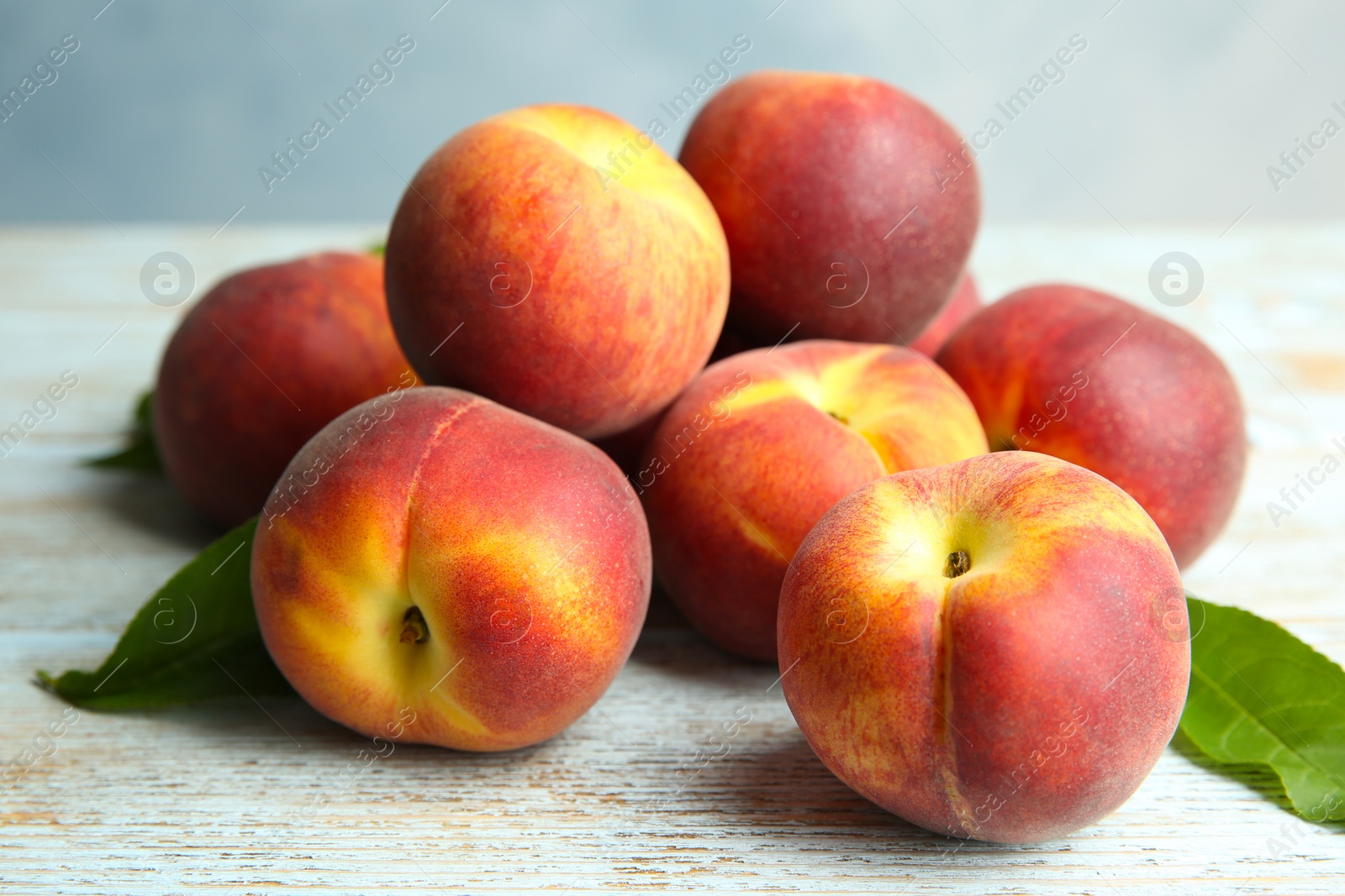 Photo of Pile of fresh peaches and leaves on wooden table