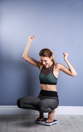 Happy young woman measuring her weight using scales on floor near color wall. Weight loss motivation