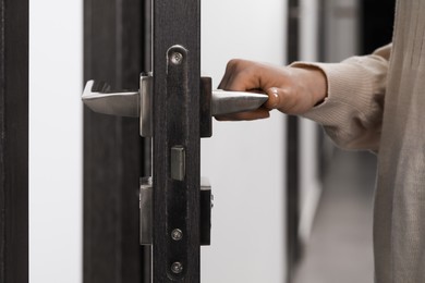 Photo of Woman opening wooden door indoors, closeup of hand on handle