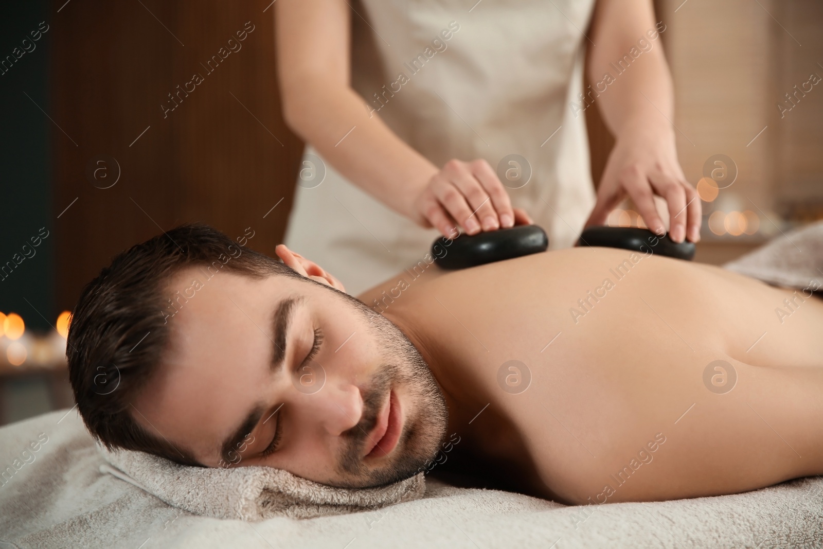 Photo of Handsome man receiving hot stone massage in spa salon