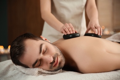 Handsome man receiving hot stone massage in spa salon