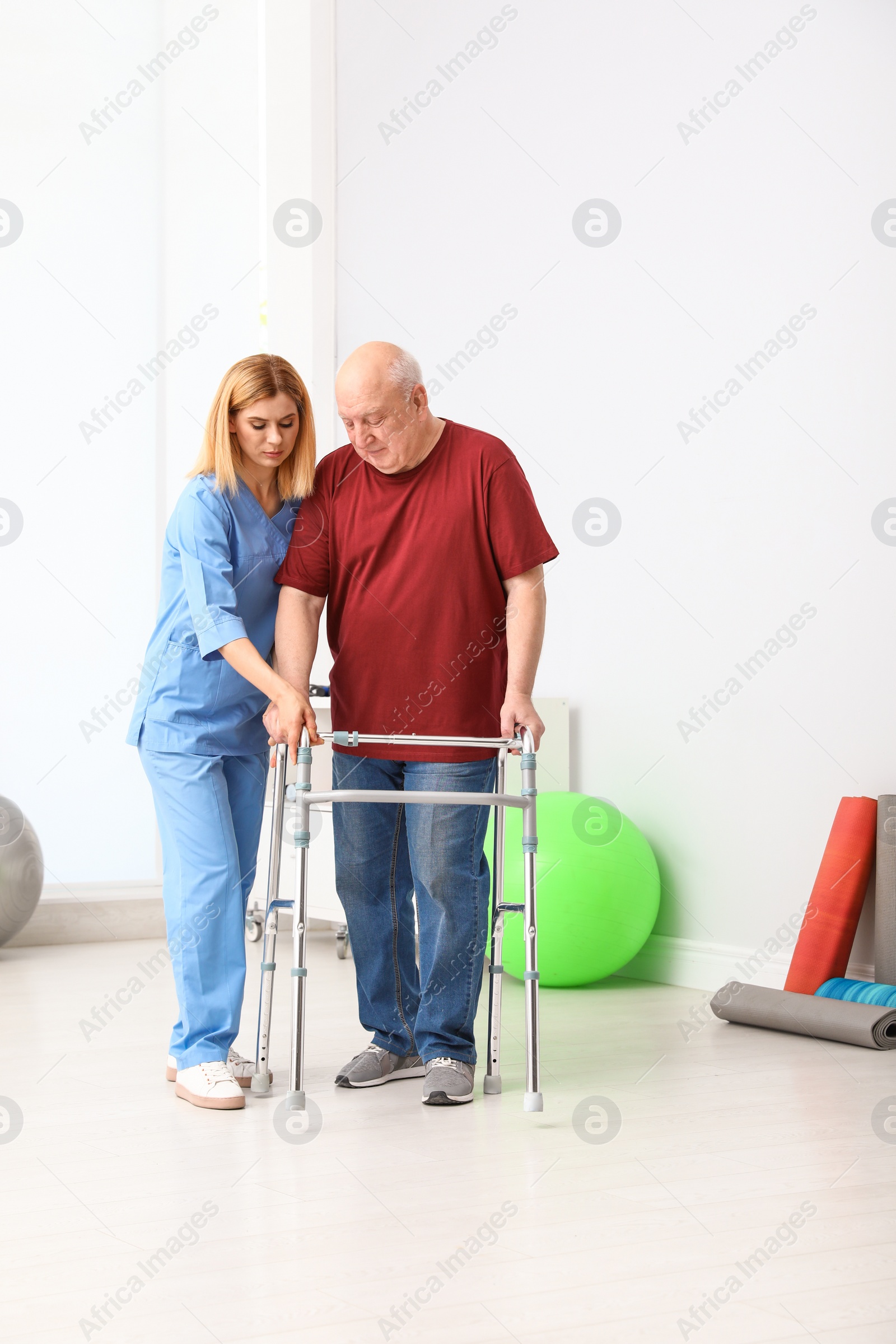 Photo of Caretaker helping elderly man with walking frame indoors