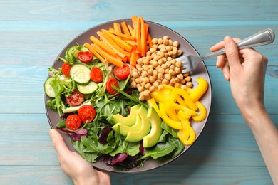 Balanced diet and vegetarian foods. Woman eating dinner at light blue wooden table, closeup