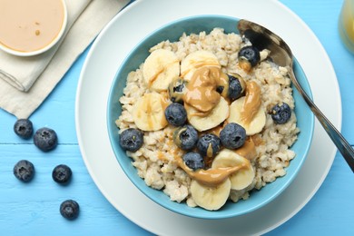 Photo of Tasty oatmeal with banana, blueberries and peanut butter served in bowl on light blue wooden table, flat lay