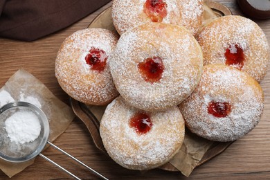 Photo of Delicious donuts with jelly and powdered sugar on wooden table, flat lay