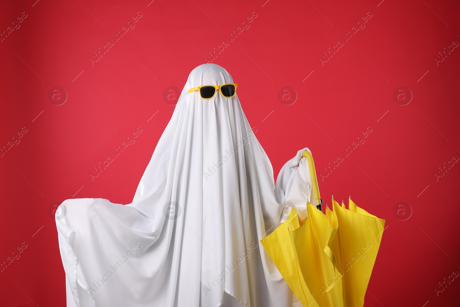 Photo of Person in ghost costume and sunglasses holding yellow umbrella on red background