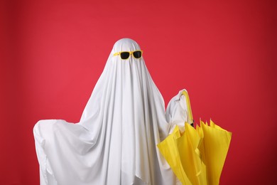 Photo of Person in ghost costume and sunglasses holding yellow umbrella on red background